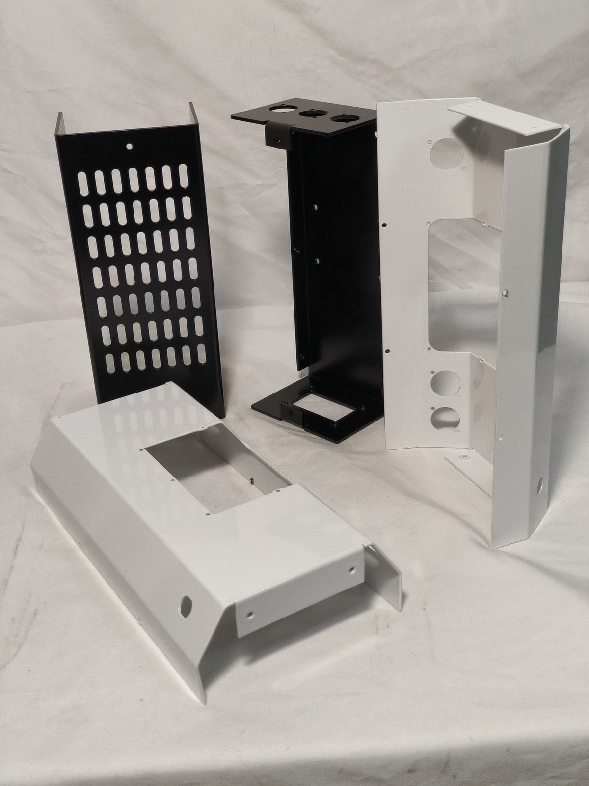 sheet metal capabilities - Black and white powder coated parts from the same production batch, including perforated panels, formed brackets and pierced covers.