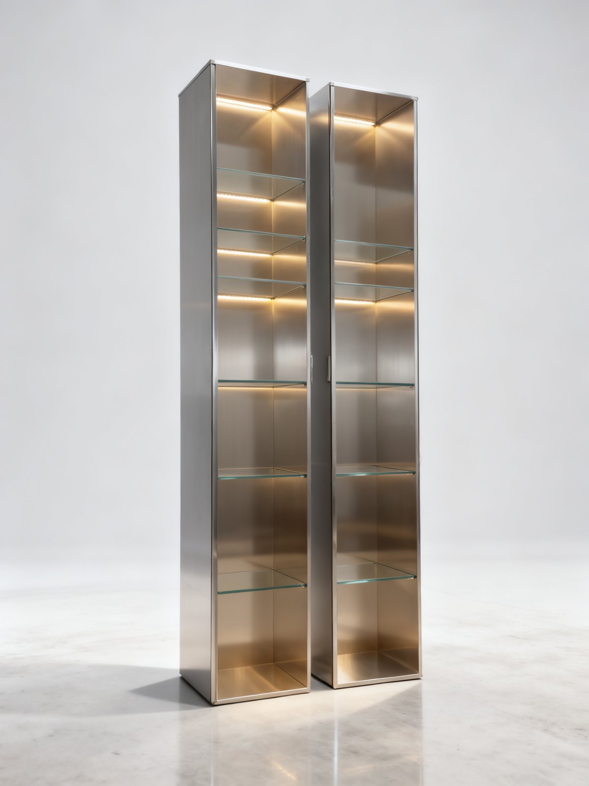 retail display cabinet - A pair of stainless steel retail display cabinets with glass shelves and warm LED lighting, photographed against a studio backdrop.